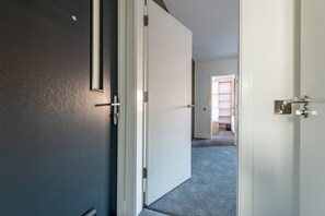A hallway with a dark door, a white door, and a carpeted floor. - Marine Place | Flat 9 (St Andrews)