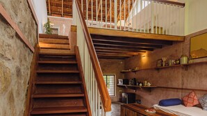 Una escalera de madera lleva a un altillo con un ventilador de techo, una cocina con refrigerador y una zona de comedor con banco.