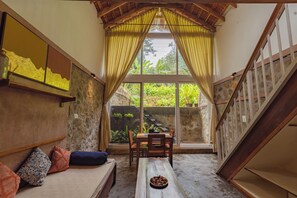 A cozy room with a stone wall, a wooden bench, a dining table with chairs, and a staircase.