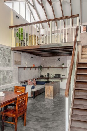 Un loft spacieux avec de hauts plafonds, un coin repas avec des meubles en bois, une cuisine Ă©quipĂ©e dâappareils modernes et un escalier avec une rampe en bois.