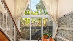 Un comedor con mesa y sillas de madera, una escalera y vistas a la vegetación a través de amplias ventanas.
