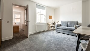 Une pièce avec un canapé gris, un bureau en bois, une chaise et un radiateur.