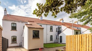 Une maison à deux étages, avec un toit en tuiles, un mur en briques et une petite cour clôturée.