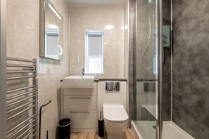 Uma casa de banho moderna com cabine de duche em vidro, lavatório com espelho e sanita.