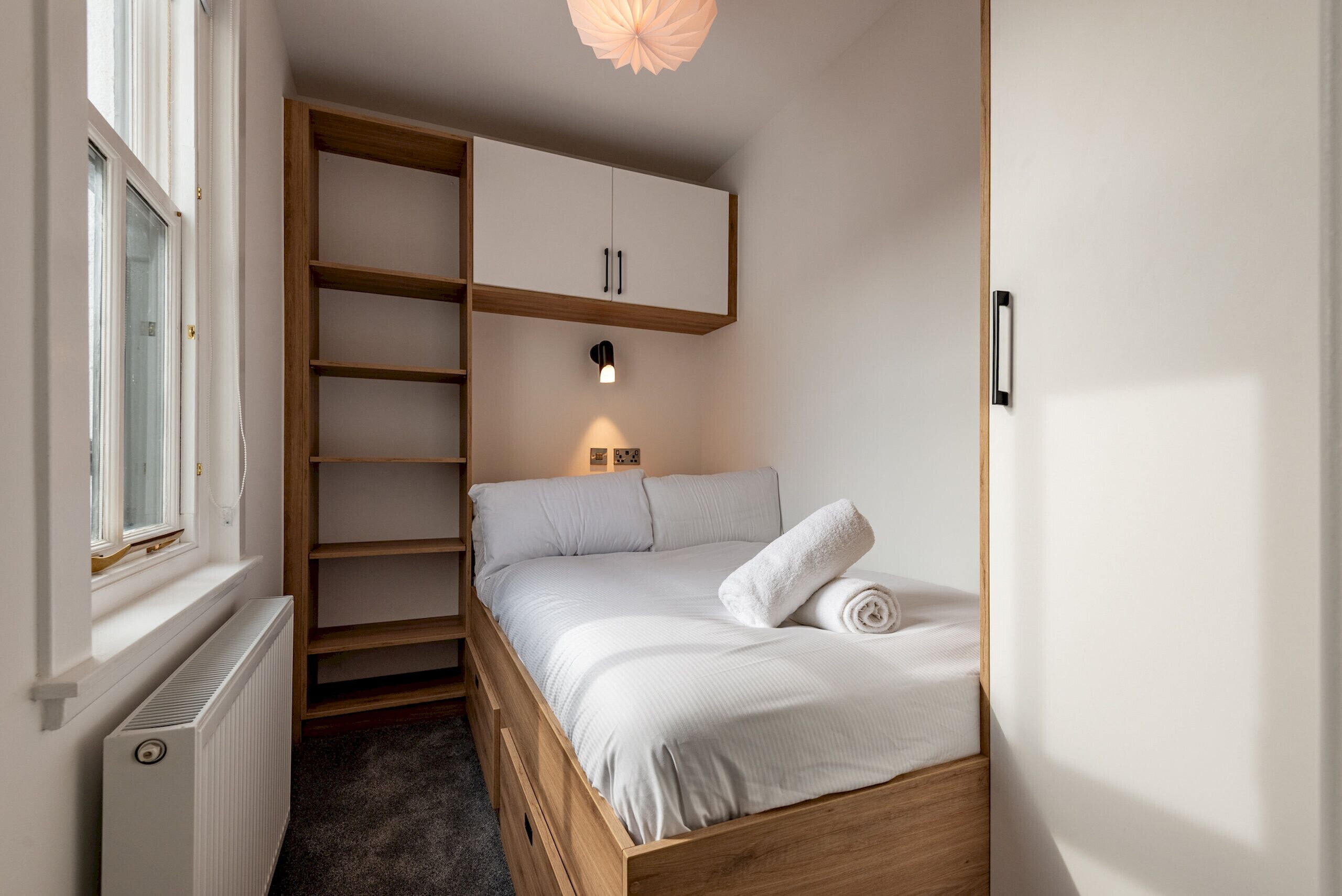 A bedroom with a bed, a wardrobe, a radiator, and a wall-mounted light.