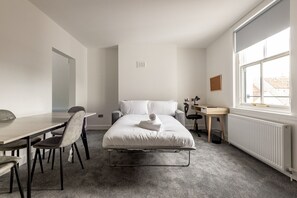 Quarto de hotel com cama, secretária, cadeira, radiador e janela.