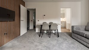 Ein modernes Wohnzimmer mit einem grauen Sofa, einem Esstisch mit vier Stühlen und einer Küchenzeile im Hintergrund.