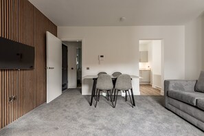 A modern living room with a grey sofa, a dining table with four chairs, and a kitchen area in the background. - Marine Place | Flat 4 (St Andrews)