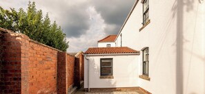 A narrow alleyway with a brick wall on one side and a white building with a tiled roof on the other. - Marine Place | Flat 4 (St Andrews)
