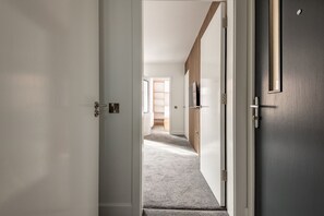 A hallway with a carpeted floor, a wooden door, and a white wall. - Marine Place | Flat 4 (St Andrews)