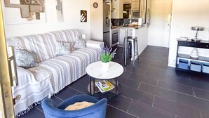 Una sala de estar moderna con un sofá, un sillón azul, una mesita redonda y una cocina al fondo.