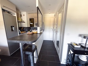 A modern kitchen with a dark countertop, stainless steel appliances, and a black bar stool.