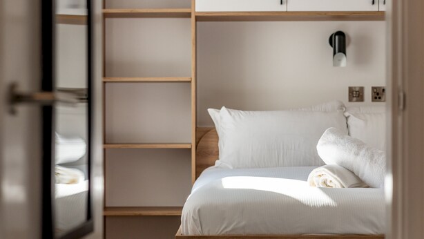 Un dormitorio con estructura de cama de madera, ropa de cama blanca y una lámpara de noche.