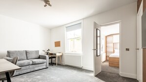 Una sala moderna con un sofá gris, un escritorio de madera y un ventanal grande.