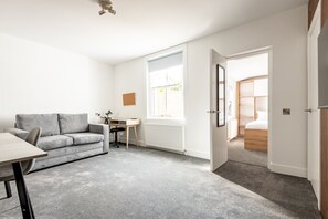 Ein modernes Wohnzimmer mit einem grauen Sofa, einem hölzernen Schreibtisch und einem großen Fenster.
