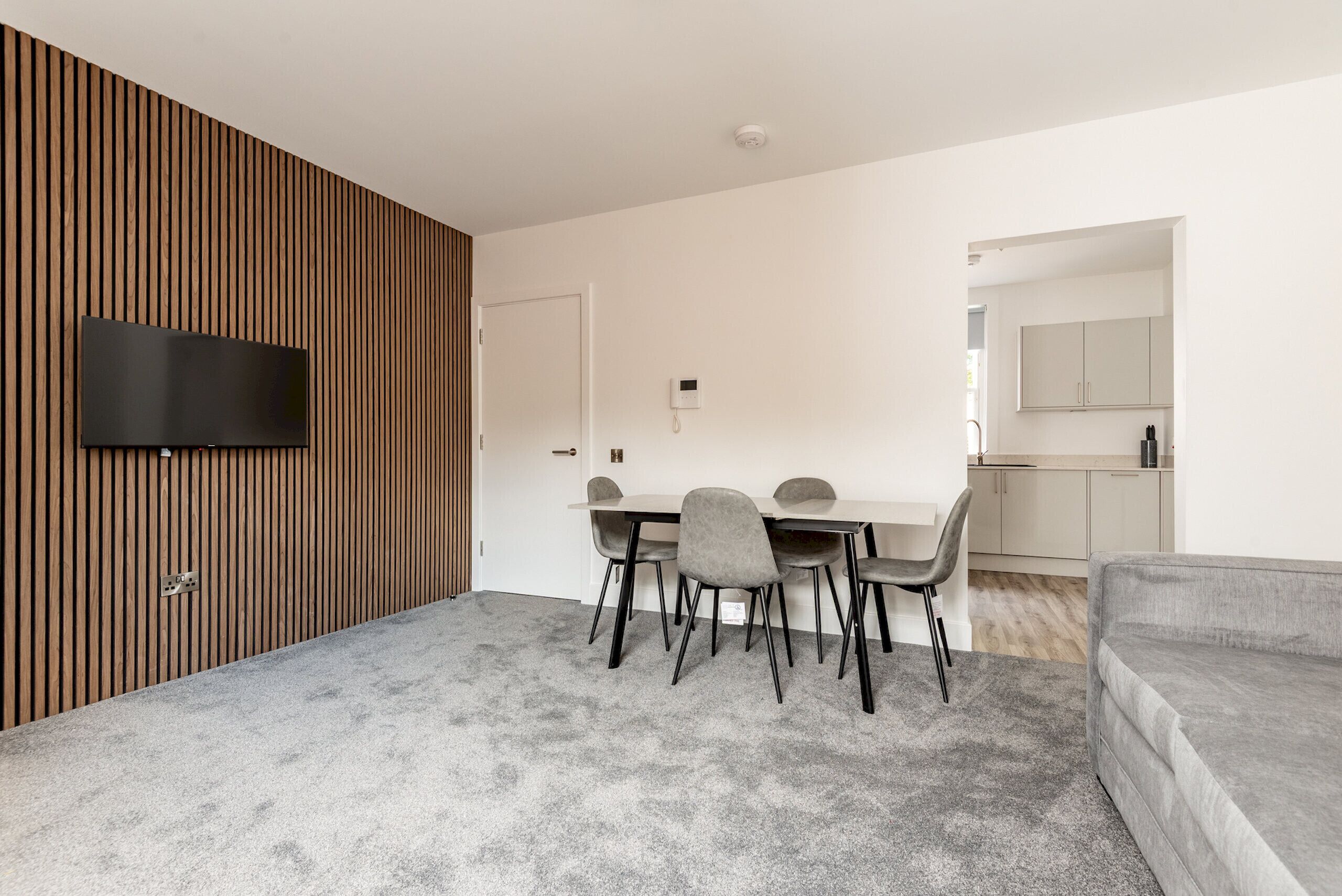 A modern living room with a flat-screen TV, a dining area with a table and chairs, and a grey sofa.