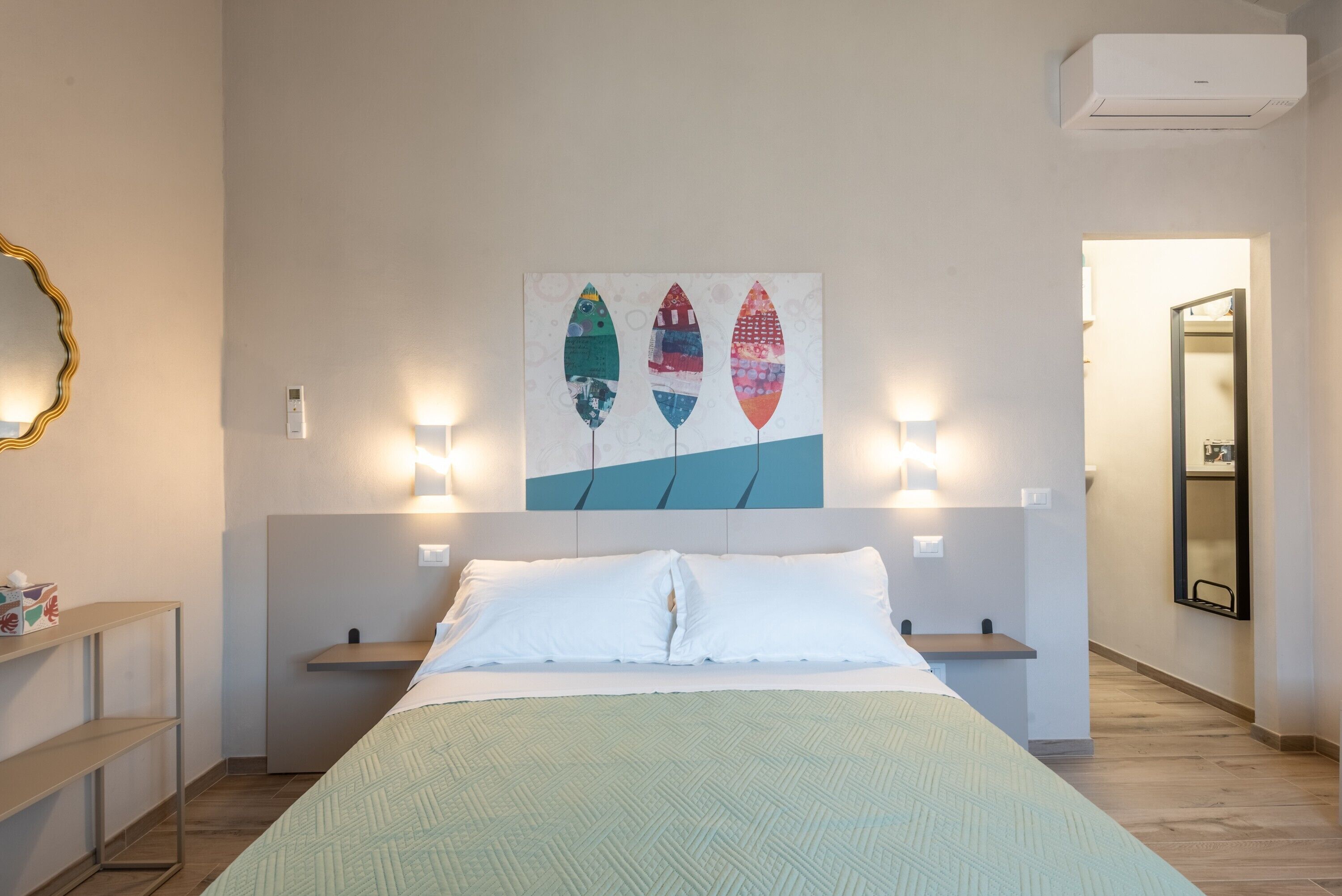 A hotel room with a bed, bedside tables, a wall-mounted artwork, and a mirror.