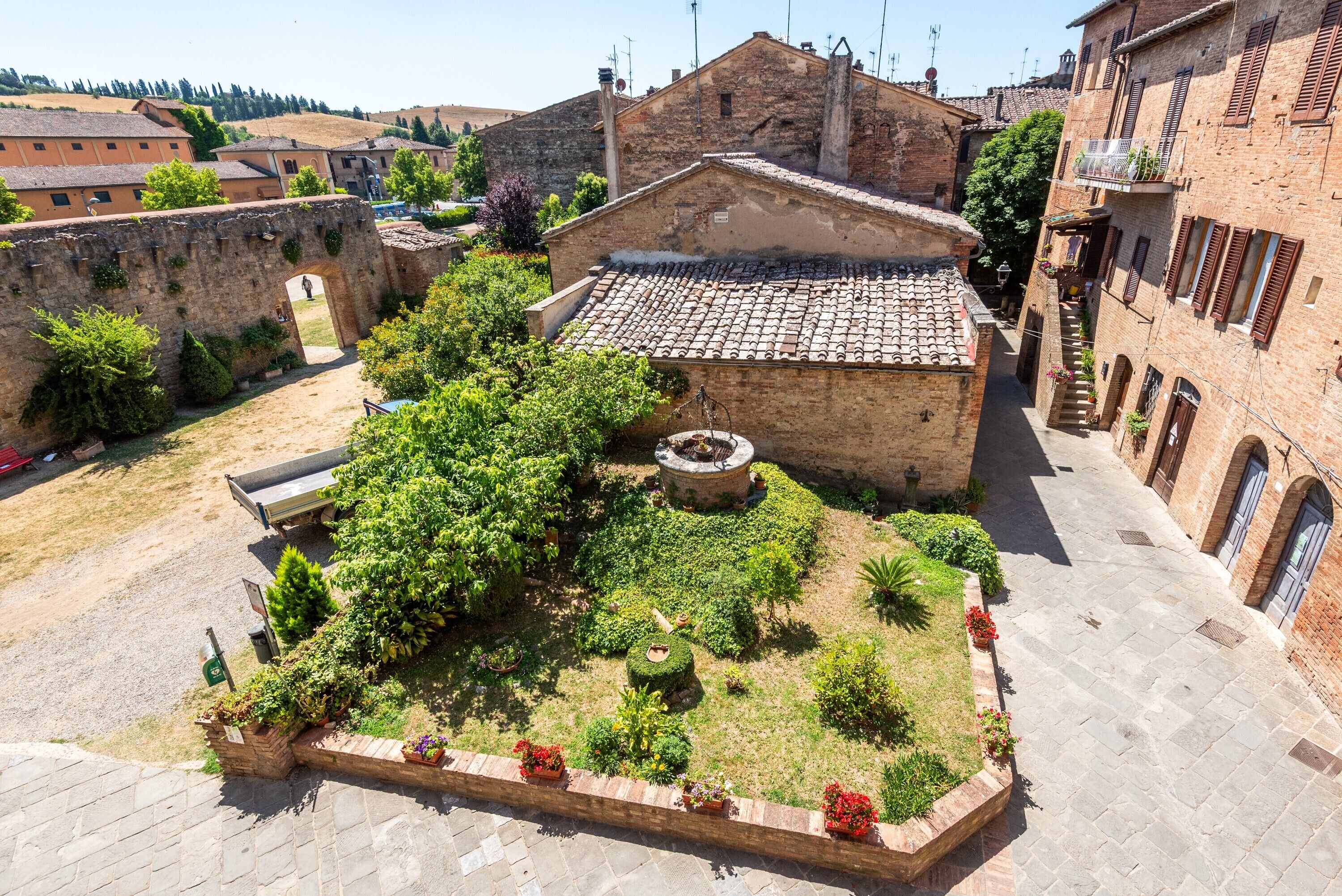 Un cortile con un edificio in pietra, un piccolo giardino e un vialetto lastricato.