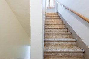 A staircase with a wooden handrail, white walls, and a window with sheer curtains. - Il Cappero Apartment in the Center of Buonconvento (Buonconvento)