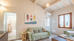 Una habitación acogedora con un sofá verde, una pequeña mesa de madera, una mesa de comedor y un cuadro en la pared.
