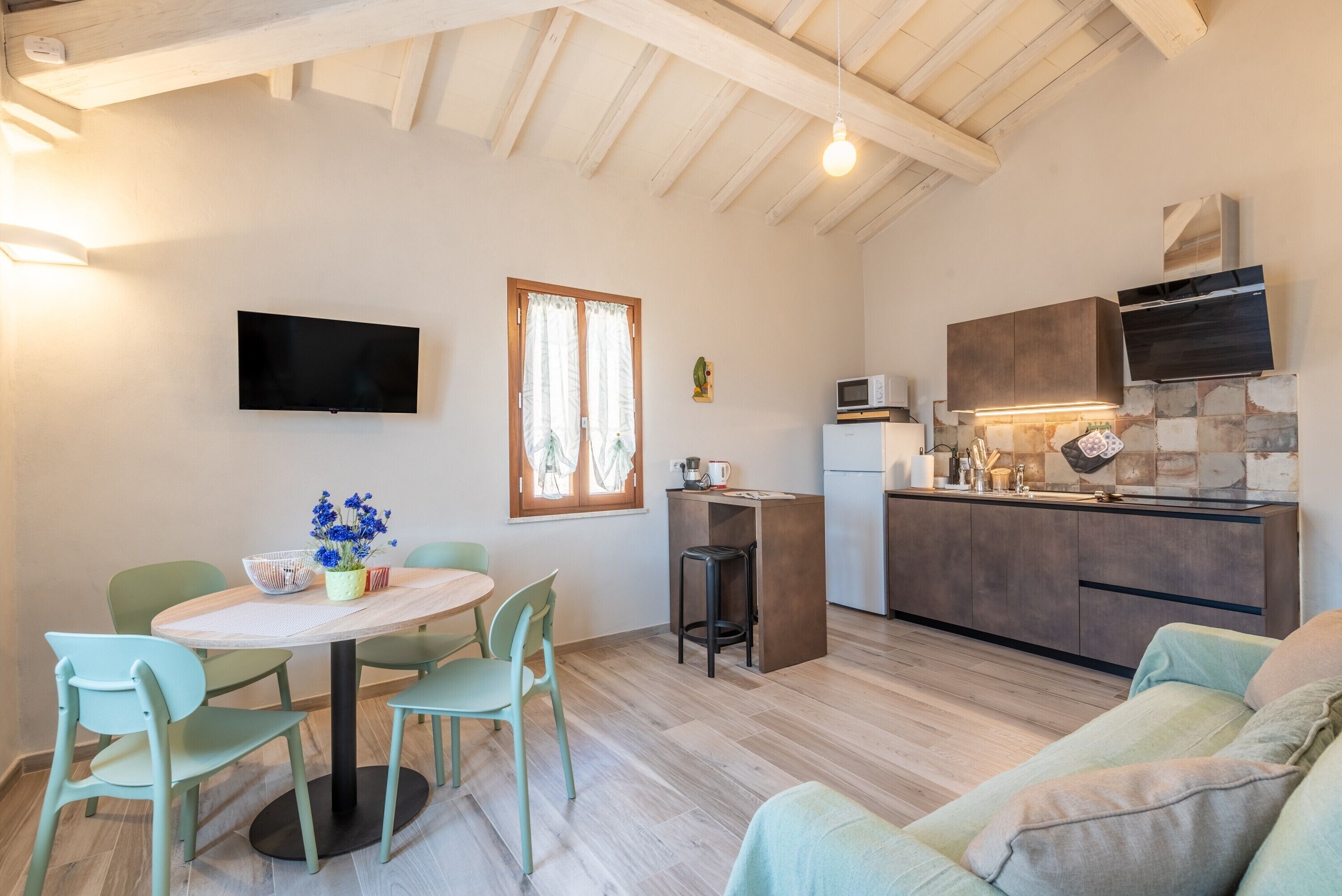 A modern kitchen with a built-in microwave, a wooden ceiling, and a dining area with a round table and chairs.