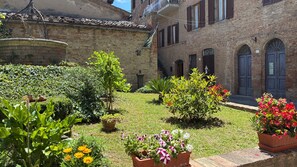 Une cour bordée de bâtiments en briques, agrémentée de plantes en pot et d’un mur de pierre.