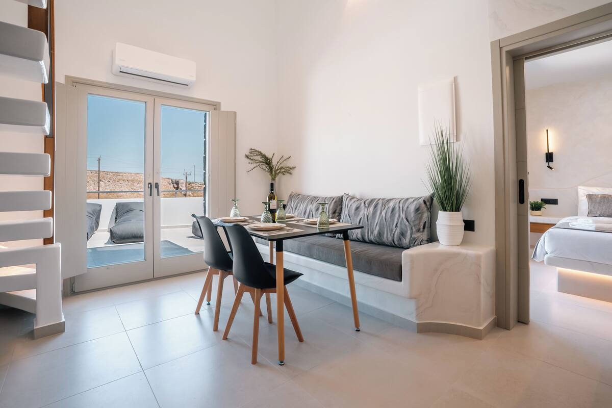 A modern room with a dining area, a sofa, a bed, and a view through a glass door.
