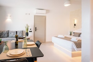 A modern hotel room with a dining area, a sofa, a bed, and a small table with a bottle and glasses.