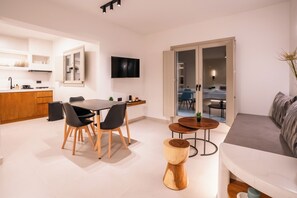 Een moderne woonkamer met een bank, een eettafel met stoelen, een aan de muur bevestigde televisie en een grote schuifpui naar een balkon.