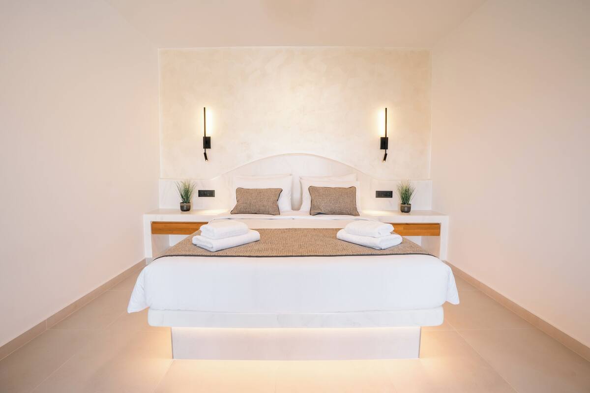 A modern hotel room with a large bed, two bedside tables with lamps, and a wall-mounted light fixture.