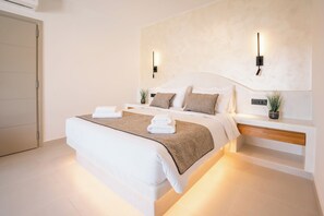 A modern bedroom with a large bed, bedside tables, wall-mounted lights, and a potted plant.