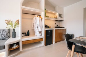 A modern kitchen with built-in appliances, a dining area with a black table and chairs, and a seating area with a bench and cushions. - Serenity Collection Suites (Santorini)