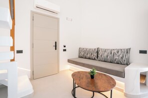 A modern room with a sofa, a round table with a plant, and a door. - Serenity Collection Suites (Santorini)
