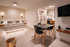A modern hotel room with a bed, bedside table, lamp, and a dining area with a table and chairs.