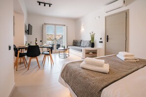 Een moderne hotelkamer met een bed, een bureau met stoelen, een bank en uitzicht op het omliggende landschap.