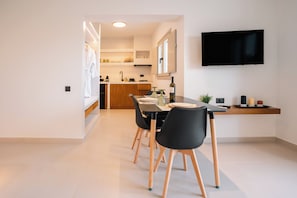 A modern dining area with a table, chairs, a TV, and a kitchen in the background.