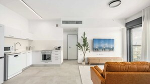 Une cuisine moderne avec des meubles blancs, un four à micro-ondes et un four encastré. On y trouve également un espace salon avec un canapé marron et une grande fenêtre.