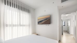 Une chambre d’hôtel avec un lit, un téléviseur fixé au mur et une vue sur la plage par la fenêtre.