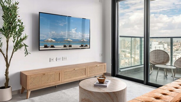 Un salon moderne doté d’un grand téléviseur, d’une console en bois, d’une table basse ronde et d’un balcon offrant une vue sur la ville.