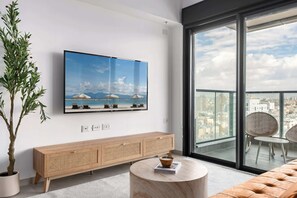 Een moderne woonkamer met een grote televisie, een houten dressoir, een ronde salontafel en een balkon met uitzicht op de stad.