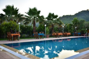 Uma piscina com cadeiras e mesas, rodeada por palmeiras e vegetação.