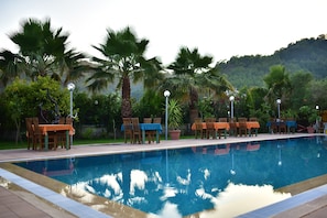 A swimming pool with chairs and tables, surrounded by palm trees and greenery.