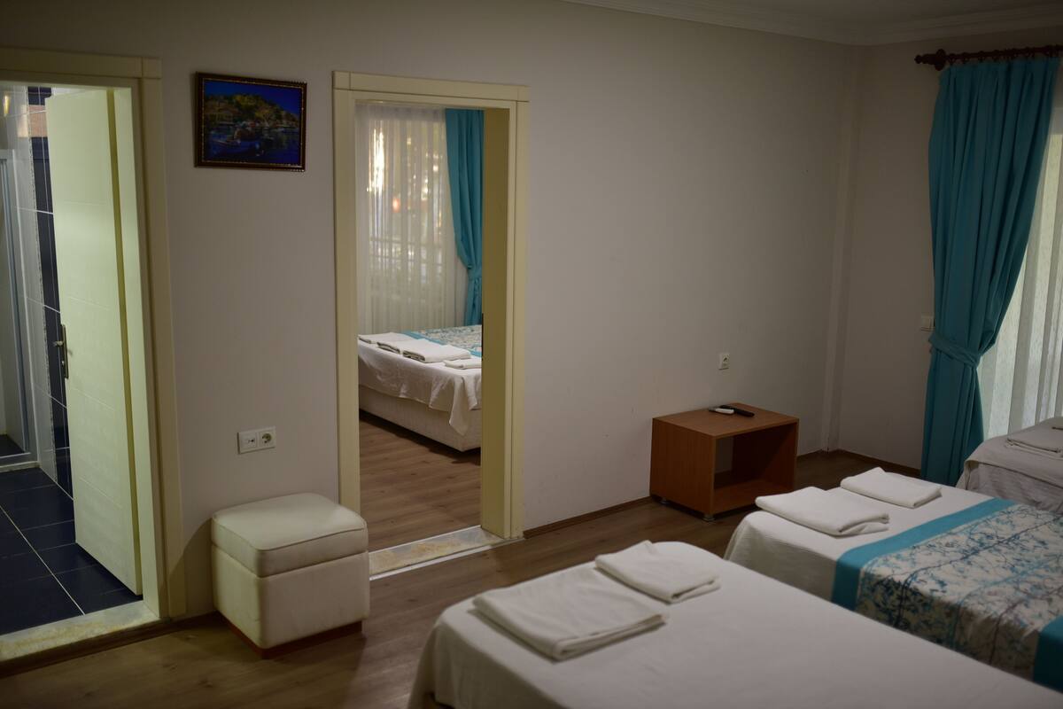 A hotel room with two beds, a small seating area, and a view through an open door.