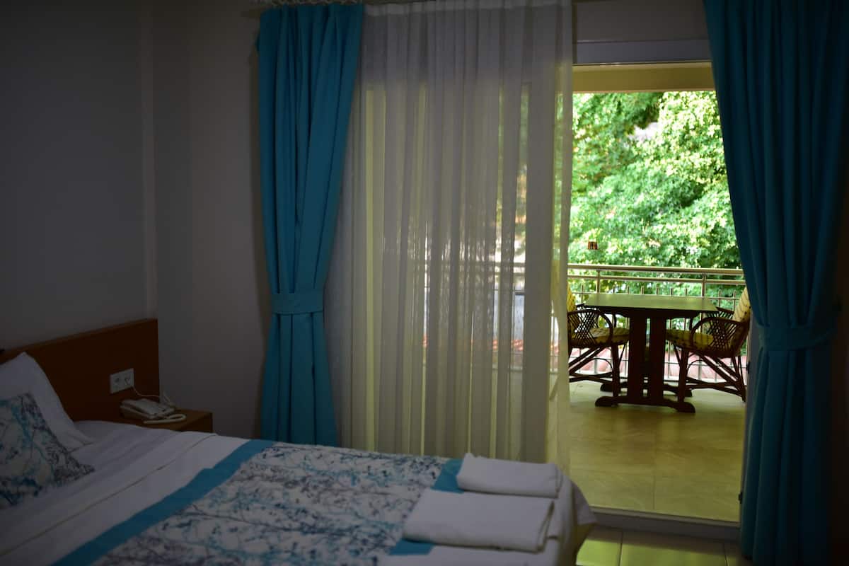 A hotel room with a bed, a telephone, a table with chairs outside, and a balcony with curtains.