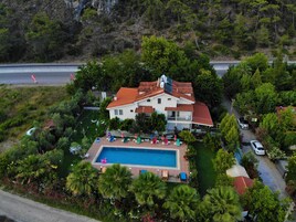 Uma casa de dois andares com piscina, rodeada por vegetação exuberante e um cenário montanhoso.