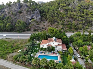Una villa con piscina, rodeada de vegetación exuberante y un promontorio rocoso.