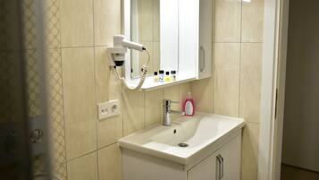 Un baño con lavamanos blanco, espejo, secador de pelo y artículos de aseo.