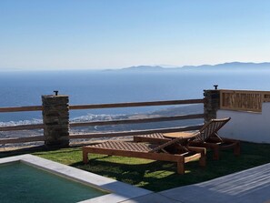 A balcony with two wooden lounge chairs, a small pool, and a view of the sea and mountains. - Felicia Exclusive Villa - Private Pool (Tinos)