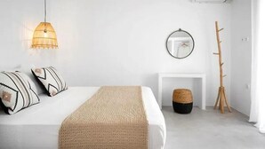 Een minimalistische slaapkamer met een bed, een hanglamp, een spiegel en een houten kapstok.