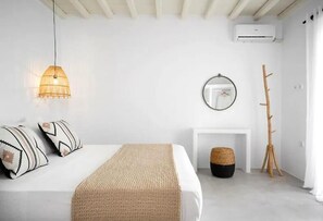 A minimalist bedroom with a bed, hanging lamp, mirror, and a wooden coat rack. - Felicia Exclusive Villa - Private Pool (Tinos)